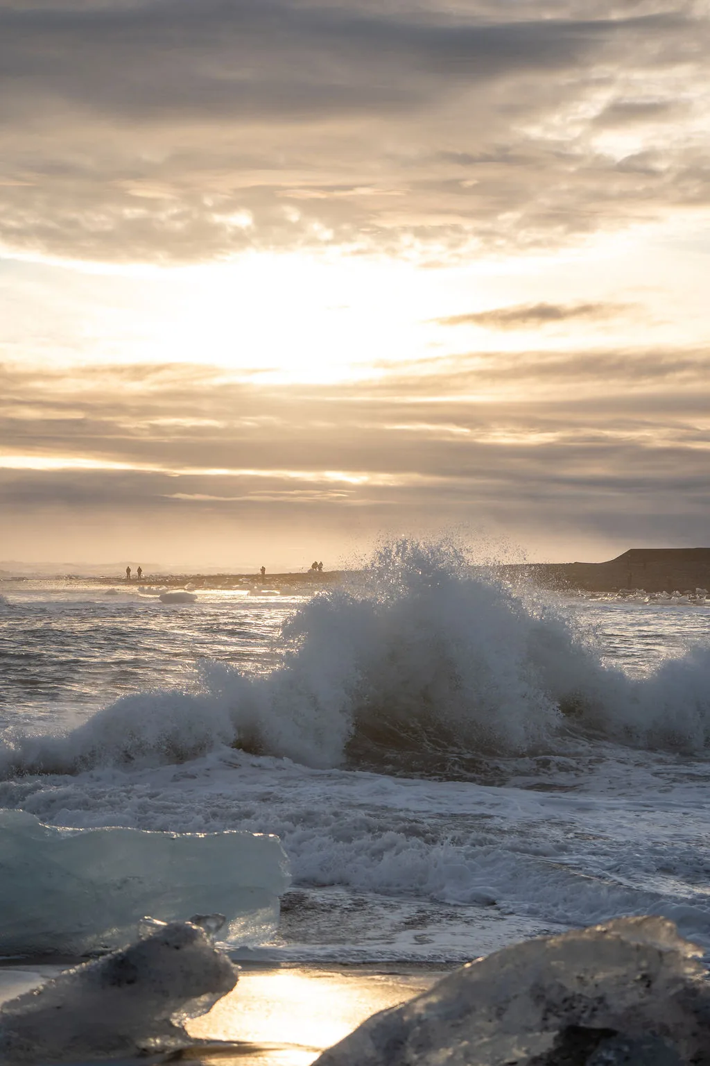 A wave breaking over ice on the black sand of Diamond Beach